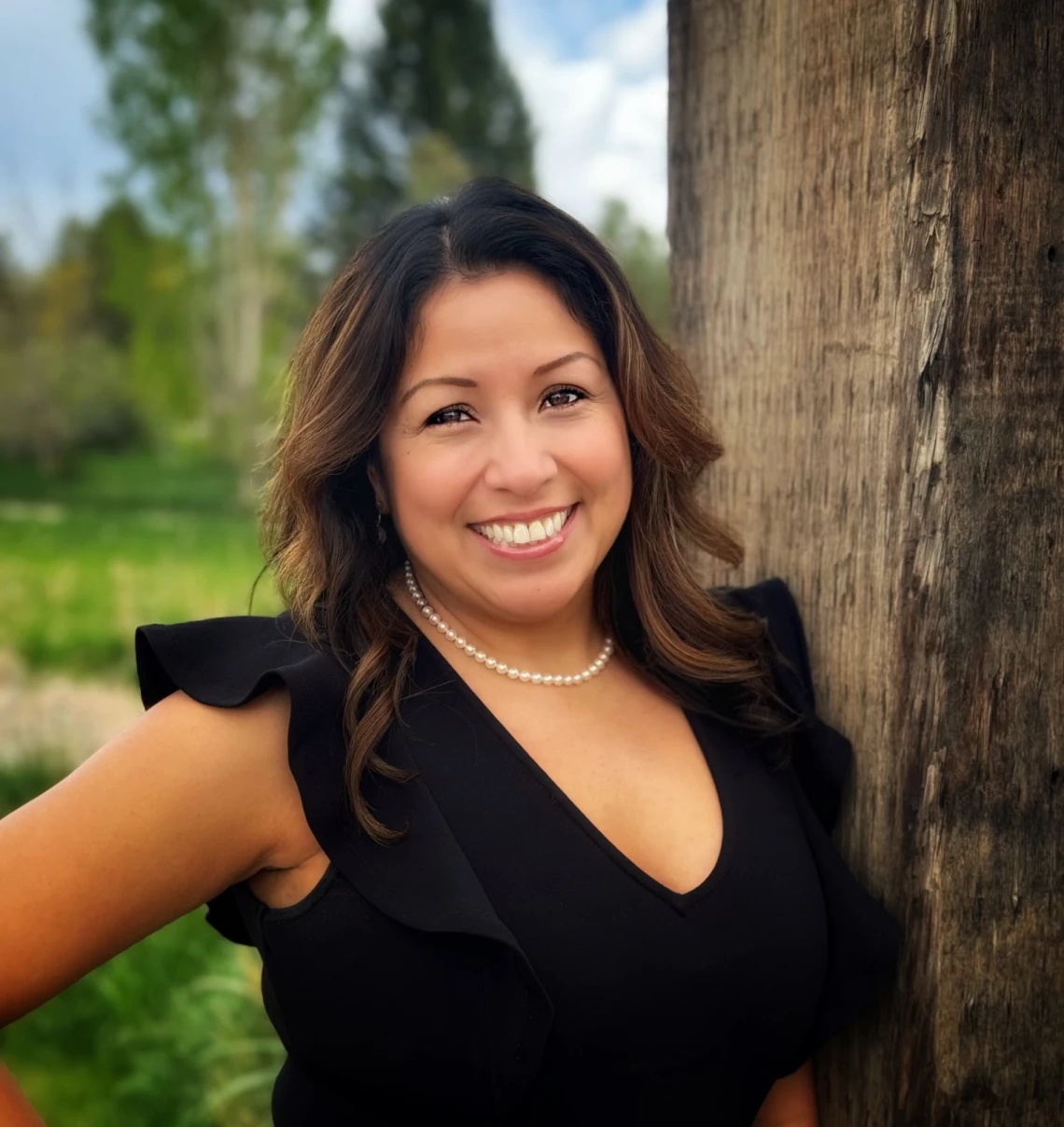 Smiling woman in black dress wearing pearls outdoors