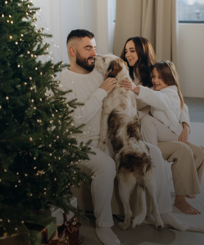 Family cuddling dog beside decorated Christmas tree