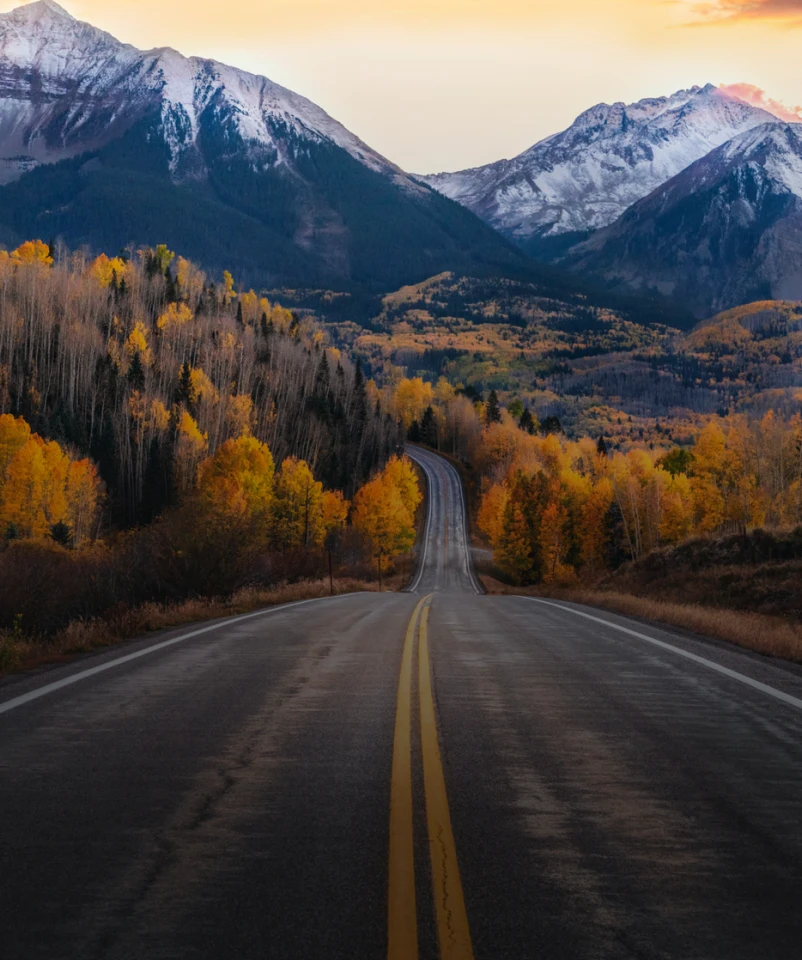 Scenic road through autumn foliage toward snow-capped mountains