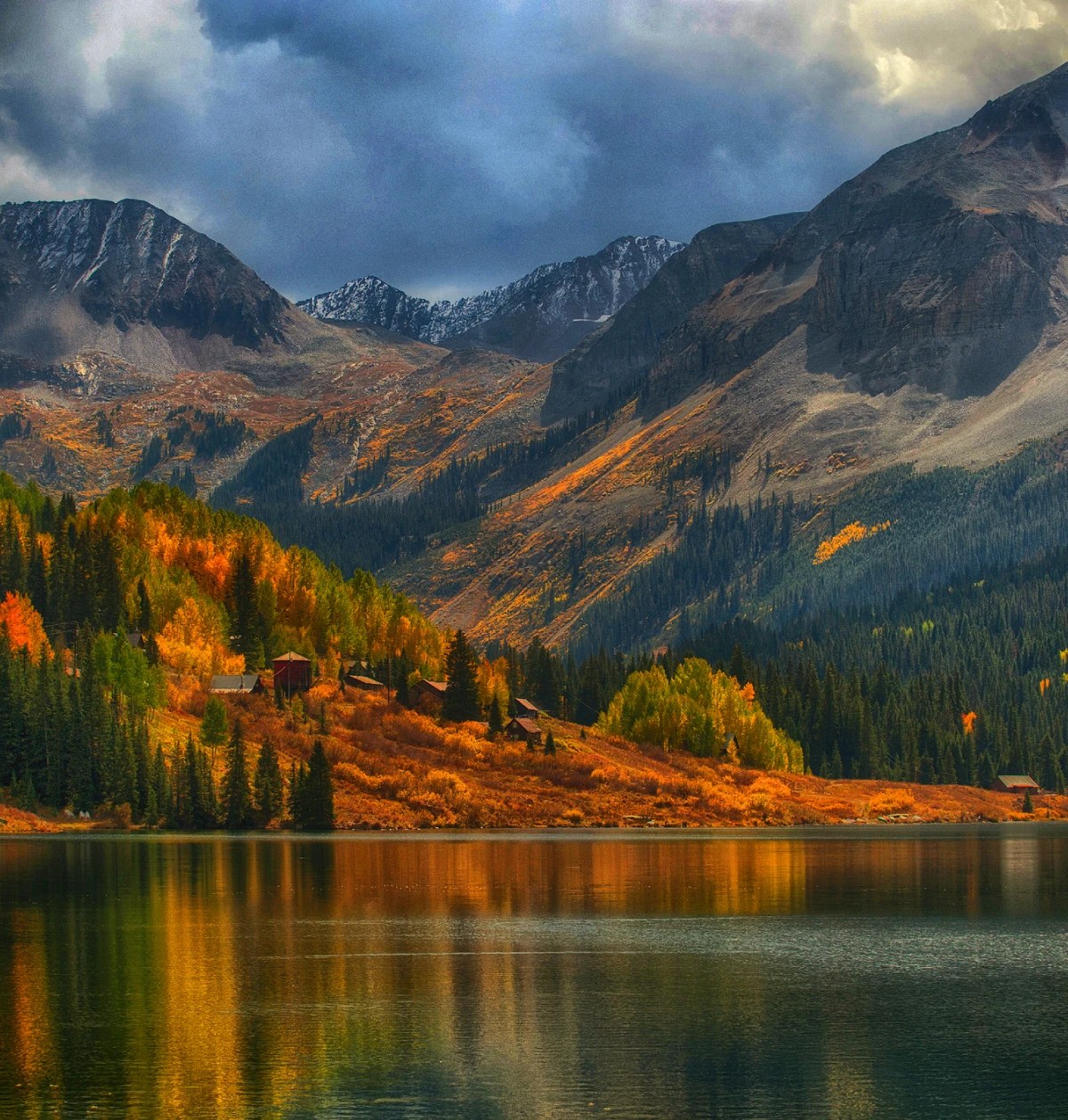Autumn lake with cabins beneath mountain peaks