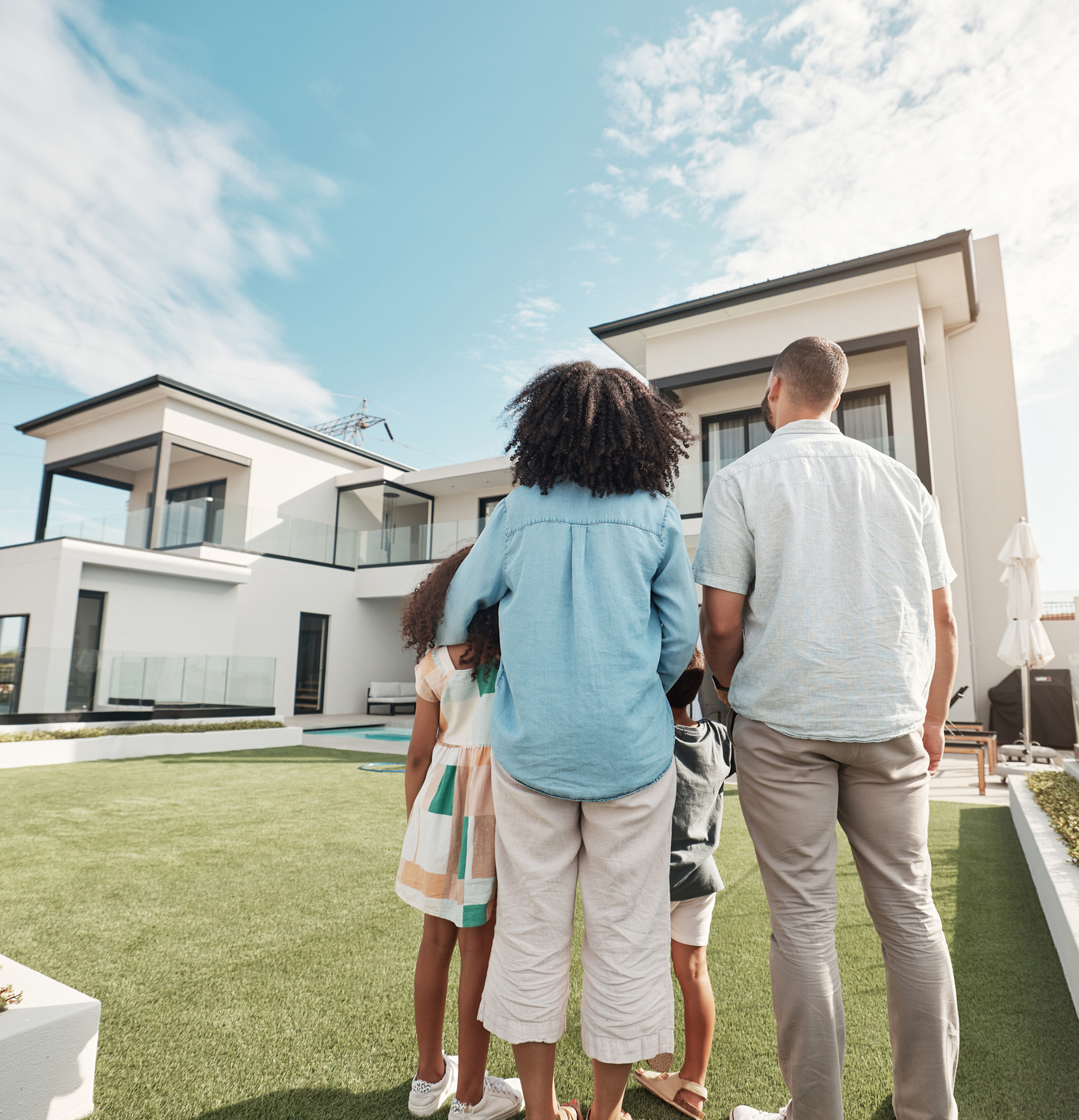 Love, new house and family in their backyard together looking at their property or luxury real estate. Embrace, mortgage and parents with their children on grass at their home or mansion in Canada.